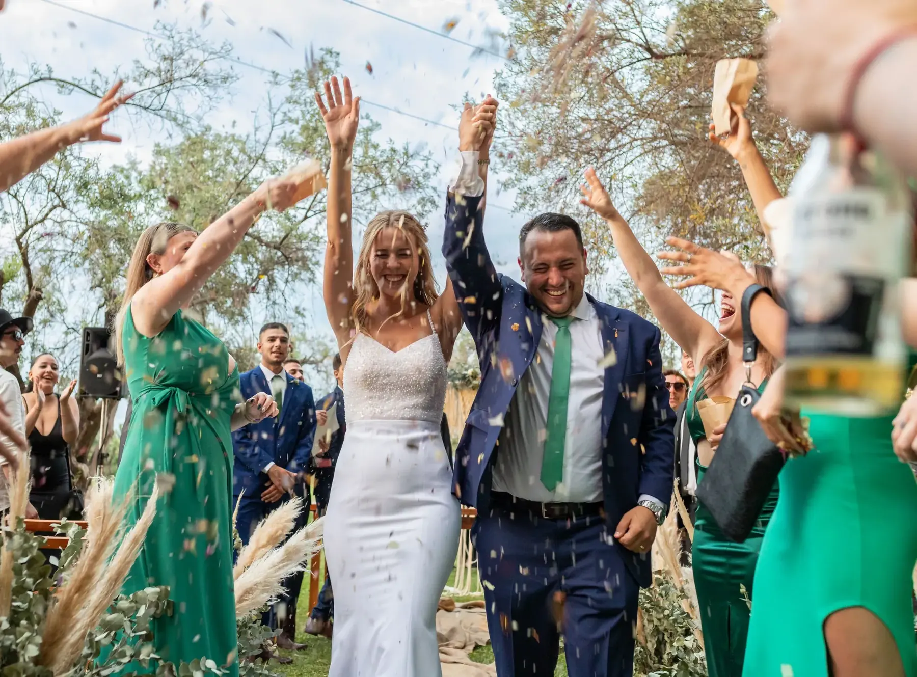 A couple walking out through confetti, their guests cheering