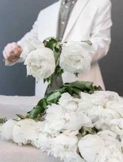 White peonies laid out on a table while a florist gathers a bunch.