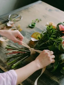 A florist's hands tie a ribbon around the stems of a bridal bouquet.