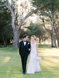 A couple walking arm in arm through parkland at dusk.